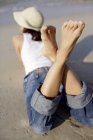 Woman in jeans and sunhat lying on front on beach, rear view. — Stock Photo
