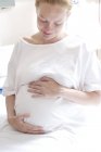 Pregnant woman at maternity ward holding swollen abdomen. — Stock Photo