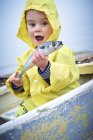 Мальчик в жёлтом плаще держит рыбу-макрель в лодке. . — стоковое фото