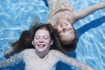 Dos chicas flotando en la piscina con los ojos cerrados, vista de ángulo alto . - foto de stock