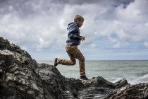 Junge im Grundschulalter rennt am Strand auf Felsen. — Stockfoto