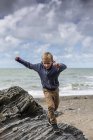 Елементарна вік хлопчик працює на скелі на пляжі. — стокове фото