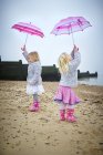 Two preschooler girls holding pink umbrellas on beach. — Stock Photo