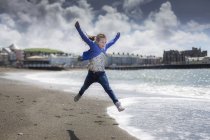 Elementary age girl leaping on sunny beach. — Stock Photo
