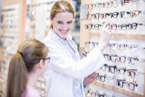 Smiling optometrist helping girl choosing glasses. — Stock Photo