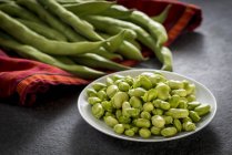 Broad beans in bowl with red towel on table. — Stock Photo