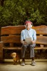 Старший чоловік сидить на лавці і слухає музику з собакою . — стокове фото