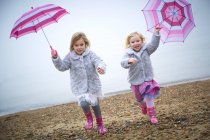 Dos niñas en edad preescolar corriendo en la playa y sosteniendo sombrillas rosadas . - foto de stock