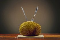 Jackfruit on table with cutlery sticking in. — Stock Photo