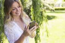 Blonde Frau schaut nach unten, benutzt Smartphone und lächelt im Freien. — Stockfoto