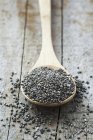 Pile of black chia seeds on wooden spoon. — Stock Photo