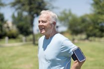 Senior man wearing smartphone on arm and earphones in park. — Stock Photo