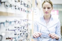 Woman holding glasses at rack in optometrist shop. — Stock Photo
