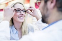 Optometrista tentando óculos na mulher na loja . — Fotografia de Stock