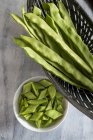 Runner beans in basket and sliced in bowl, high angle view. — Stock Photo