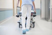Enfermeira homem ordenadamente empurrando cama no corredor . — Fotografia de Stock