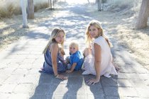 Mother with toddler son and daughter sitting on park path and looking back. — Stock Photo
