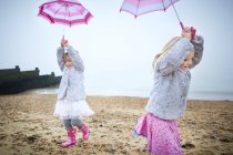 Two preschooler girls walking on beach and holding pink umbrellas. — Stock Photo