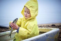 Niño pequeño en impermeable amarillo sosteniendo pez caballa en barco . - foto de stock