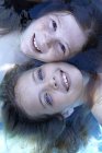 Portrait of two elementary age girls floating in water, high angle view. — Stock Photo