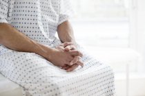 Male patient wearing hospital gown and sitting on bed. — Stock Photo