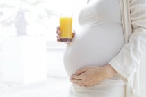 Беременная женщина со стаканом фруктового сока трогает животик . — стоковое фото