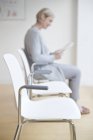 Жінка сидить у залі очікування лікарні та читає журнал . — стокове фото
