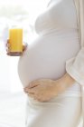 Femme enceinte avec un verre de jus de fruits touchant le ventre . — Photo de stock