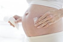 Pregnant woman moisturizing tummy with cream — Stock Photo