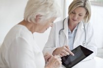 Ärztin zeigt Seniorin Röntgenbild der Hand auf digitalem Tablet. — Stockfoto