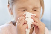 Elementary age girl sneezing into tissue. — Stock Photo