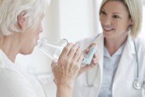 Senior woman using inhaler with female doctor watching. — Stock Photo