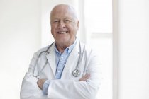 Senior male doctor with arms crossed smiling and looking in camera. — Stock Photo