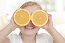 Ragazza in età elementare che tiene le arance sugli occhi . — Foto stock
