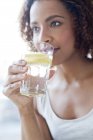 Frau trinkt Wasser mit einer Scheibe Zitrone. — Stockfoto