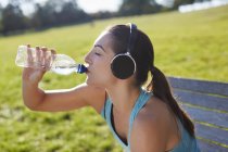 Молода жінка в навушниках п'є воду . — стокове фото