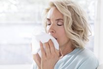 Mature woman blowing nose on tissue. — Stock Photo