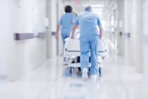 Médicos empujando cama de hospital con paciente a través del pasillo . - foto de stock