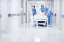 Médicos empurrando cama hospitalar com paciente através do corredor . — Fotografia de Stock