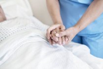 Медсестра держит пациента за руку в больничной койке . — стоковое фото