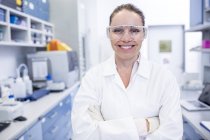 Женщина лаборантка в защитных очках стоит со скрещенными руками . — стоковое фото