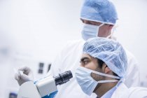 Científicos masculinos en tapones quirúrgicos usando microscopio . - foto de stock