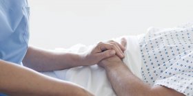 Жіноча медсестра тримає чоловічу руку пацієнта в лікарняному ліжку . — стокове фото