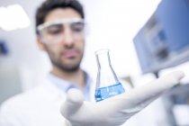 Мужчина лаборант держит химическую фляжку . — стоковое фото