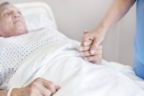 Enfermera sosteniendo mano de paciente mayor en cama de hospital . - foto de stock