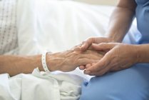 Медсестра тримає чоловічу руку пацієнта в лікарняному ліжку . — стокове фото