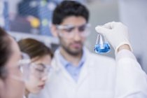 Auxiliares de laboratório olhando para frasco químico com líquido azul . — Fotografia de Stock