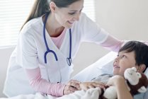 Niño en cama de hospital con una enfermera sonriente . - foto de stock