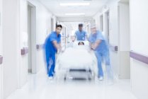 Medici che spingono letto d'ospedale con il paziente attraverso il corridoio . — Foto stock