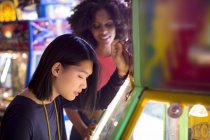 Female friends playing arcade game at fun fair. — Stock Photo